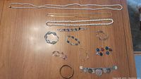 Photo showing three necklaces (two faux knotted pearl and one gold-tone) laid out on a wooden surface with nine assorted bracelets arranged below them.