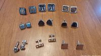 Nine pairs of cuff links with varied design and materials, displayed on a wooden surface.