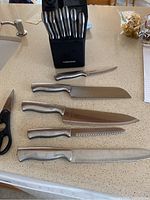Photo showing Farberware knife block, six knives with stainless steel handles laid out on counter.