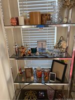 Photo showing assorted candles, glass vases, wicker basket, shell decoration, picture frames and small decorative objects on a metal shelf.