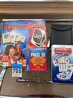 Photo showing Rummikub Classic game, Uno cards, Phase 10 cards, and Mexican Train Dominoes set on a shelf.
