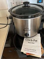 Rival Crock-Pot slow cooker, stainless steel finish with glass lid and front rotary knob, includes owner's guide/manual.