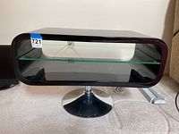 Front view showing black acrylic frame with glass shelf inside and chrome metal base