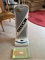Front view of Oreck XL Xtended Life upright vacuum showing fabric bag with branding and included extra vacuum bags lying flat in front.