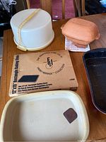Shows Pampered Chef stoneware baking dish, baking stone in box, terracotta covered baker, vintage Tupperware cake carrier on wooden table