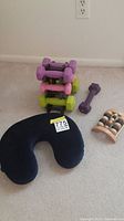 Neck pillow in front with stacked colorful dumbbells, loose purple dumbbell, and wooden foot massager visible.