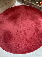 Top view of the round red wool area rug showing the color and subtle embossed border design.