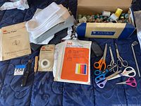 Wide view showing box with sewing threads, scissors, tracing papers, fabric scraps, and sewing tools on a bedspread.