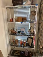 Full view of tall glass and chrome etagere with four glass shelves, reflective chrome metal frame. Shelf contents visible but not included.