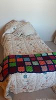 Twin bed fully made with floral comforter, multiple pillows, and crocheted afghan at foot of bed.