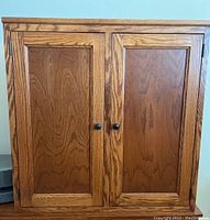 Front view of the closed cabinet showing wood grain and two paneled doors with knobs.