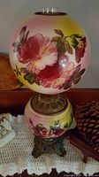 Antique oil lamp showcasing the floral hand-painted glass globe with pink and yellow flowers and ornate metal base.