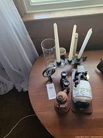 View of all items on a round table by window including candles, candle holders, binoculars, coffee grinder, and oil lamp