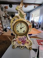 Front view of the porcelain clock with floral design on the case and ornate golden bezel.
