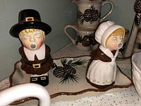 Close-up of vintage Pilgrim man and woman salt and pepper shakers on a tray with pinecone motif