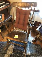 Wooden mid-century modern rocking chair with floral inlay on top rail and tufted brown cushion tied to backrest. Chair is medium brown wood with spindle back and curved rockers.