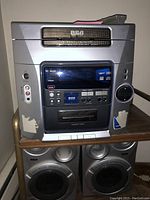 Front view of RCA 5 disc CD changer stereo on metal and wood stand with two RCA speakers below