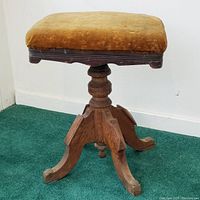 Side view of antique wooden stool showing square yellow velvet upholstered seat and carved wooden legs with central turned support.