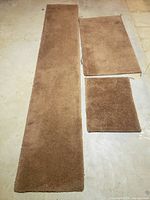 Photo of three brown carpet remnants arranged on a concrete floor, showing the full set size differences.
