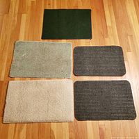 Five rectangular mats displayed on wood floor; includes dark green, light green, off white, and two grey mats.