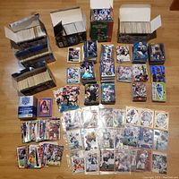 Multiple boxes and stacks of football cards with loose and set-organized cards laid out on floor, showing wide variety of cards and players.