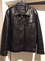 Front view of men's Guess black leather jacket showing full zipper, chest zip pocket, collar and side pockets.