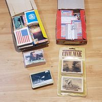 Top view of multiple boxes and smaller sets of military-themed trading cards laid out on wooden floor.