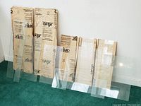 13 panes of glass displayed leaning against a wall, 5 are sealed in paper packaging showing the brand 'Optix' with visible dimensions.