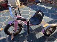Pink children's tricycle with black seat, chrome fenders and black handle grips, showing front and side views.