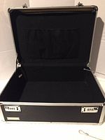 Open view of the black metal storage lock box showing the interior black fabric lining and mesh pocket inside the lid.