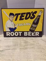 Rectangular yellow metal sign with Ted Williams baseball player and Ted's Root Beer bottle graphics.