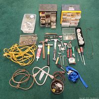 Full view of assorted tools, hardware containers, extension cords, and electrical supplies arranged on the floor.
