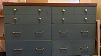 Front view of 6 drawer dresser showing blue paint, mixed hardware knobs and pulls, and wood top with minor wear.
