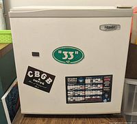 Front view of one white Haier mini bar fridge with stickers on door including green '33' oval sticker and CBC sticker