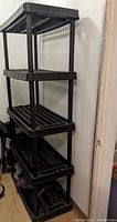Black 4-shelf resin/plastic storage rack with slatted shelves and tubular legs, shown against a wall.