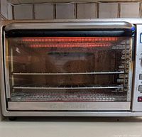 Front view of Black & Decker stainless steel digital convection toaster oven turned on, showing heating elements inside and interior rack setup.