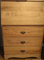 Front view of solid wood desk showing three drawers, one missing handle, natural finish.