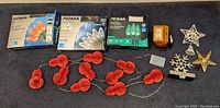 Holiday string lights in original packaging and red bulb lights laid out, decorative star and snowflake light covers, a strobe light in orange casing