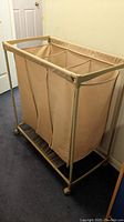 Rolling 3-section laundry hamper with metal frame and beige fabric compartments on caster wheels