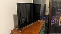 Samsung 32-inch LED Smart TV viewed from side on a wooden table near glass door.