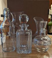 Image shows four different clear glass decanters including a square spirit decanter with a crystal-like faceted stopper, a round bottle with an apple shaped stopper, and two other clear glass decanters. All clear glass and in very good condition.