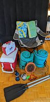 Camping and beach gear including two coolers, camping chair, rolled sleeping bags, oars, lanterns, grill rack, beach towels, and beach toys visible