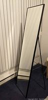 Black frame standing full-length IKEA KARMSUND mirror angled against wall
