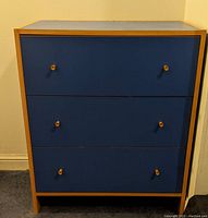 Front view of blue dresser with three drawers and natural wood trim