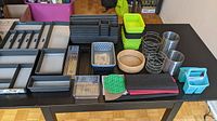 Wide view of all storage containers, bins, baskets, liners, and wire holders arranged on a black table.