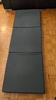 Tri-folding memory foam sleeping pad, dark colored with some wear and pilling on removable cover folded out flat on floor.