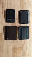 Overview of 4 wallets on wooden surface: two black leather wallets on top, brown textured wallet bottom left, black smooth wallet bottom right.