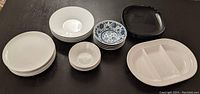 Wide shot of all dinnerware items on a dark surface showing various bowls, plates, and platter.