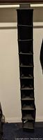 Tall black hanging closet organizer with ten shelves hanging vertically in closet.