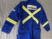Full back view of the blue flame resistant Westex coveralls with yellow reflective stripes forming an 'X' and a TRAILBLAZER DRILLING CORP patch on the upper back.